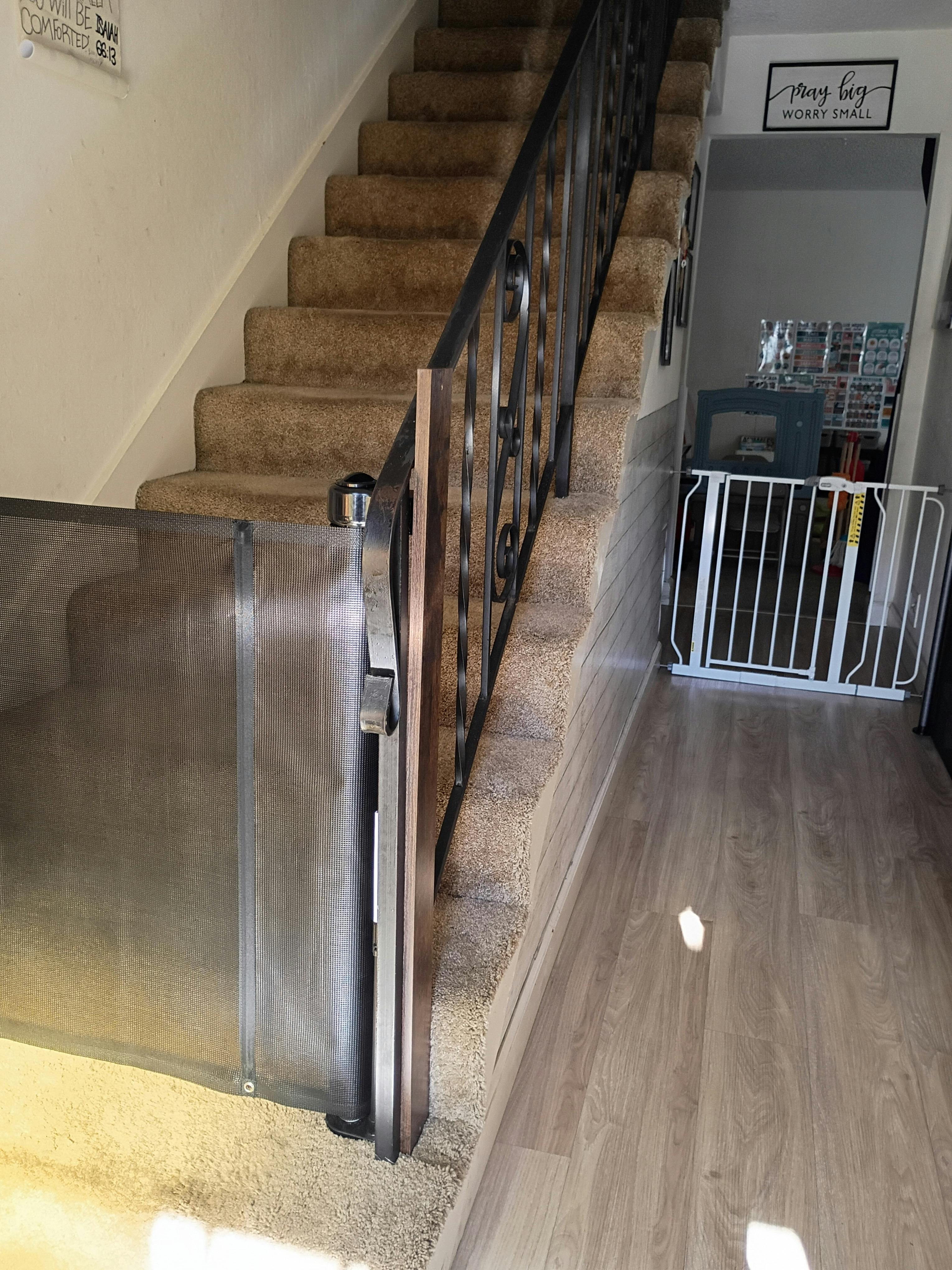 Retractable safety gate mounted at the top of a carpeted staircase