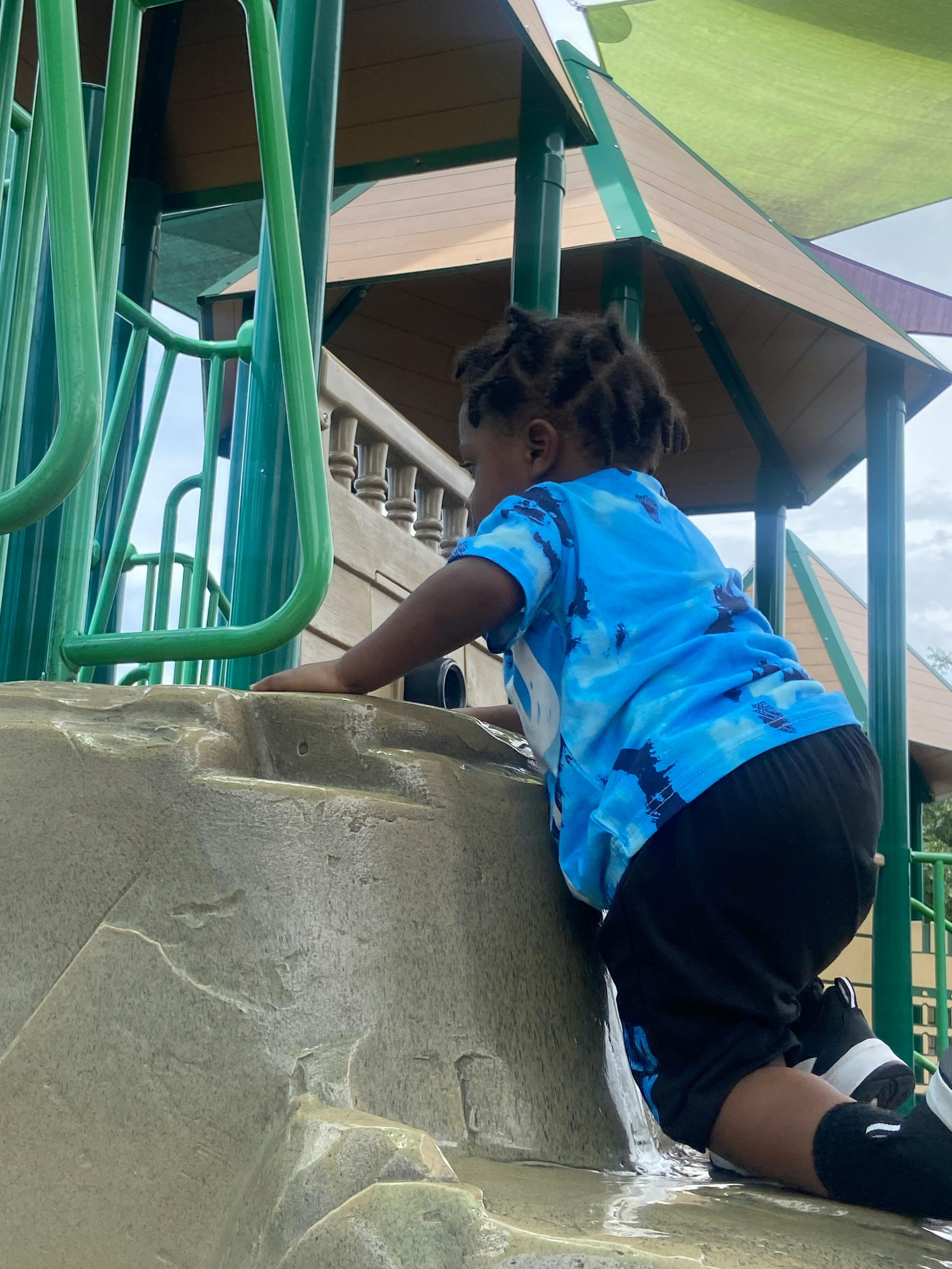 Child crawling up a green and tan playground slide