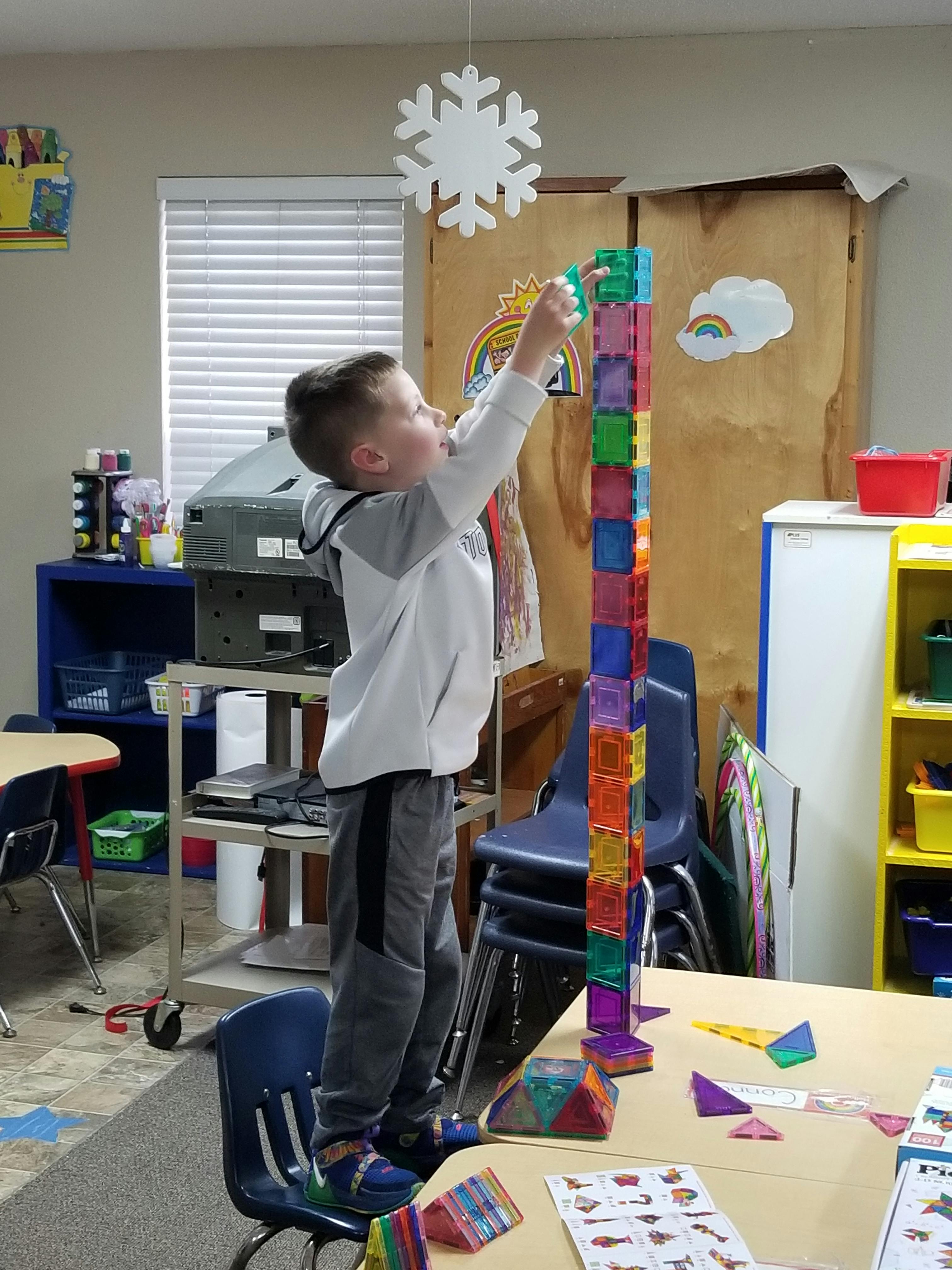 Child standing on a chair building a tall tower with colorful blocks