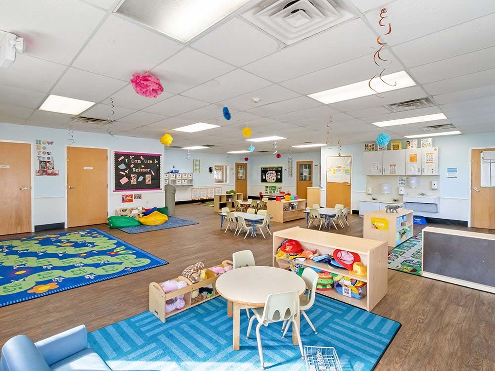 Empty colorful preschool classroom with small tables, chairs, and play areas
