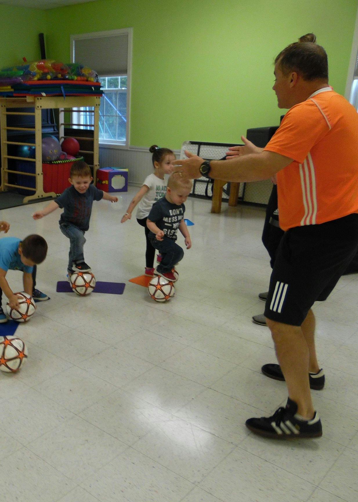 Adult instructing children balancing on soccer balls in a classroom
