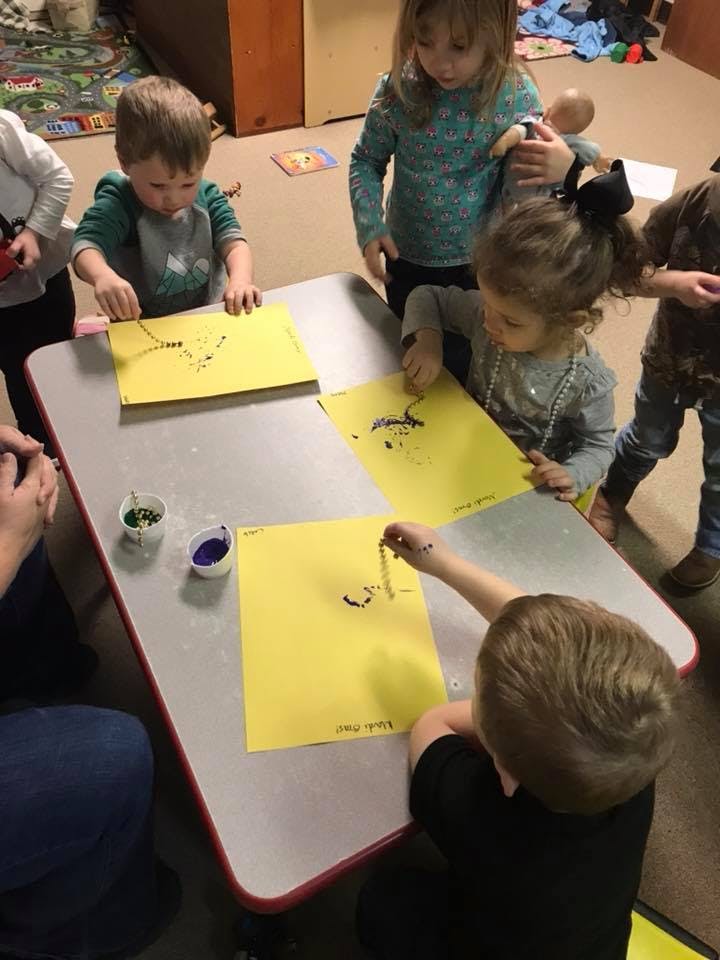 Children making art with paint on yellow paper at a table