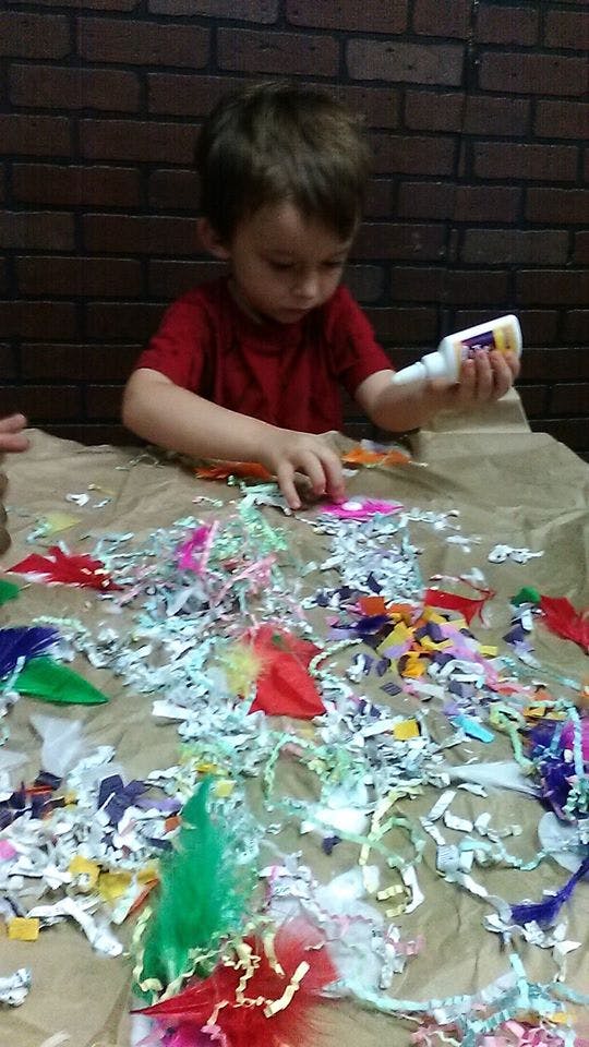 Child holding a glue bottle over colorful craft materials