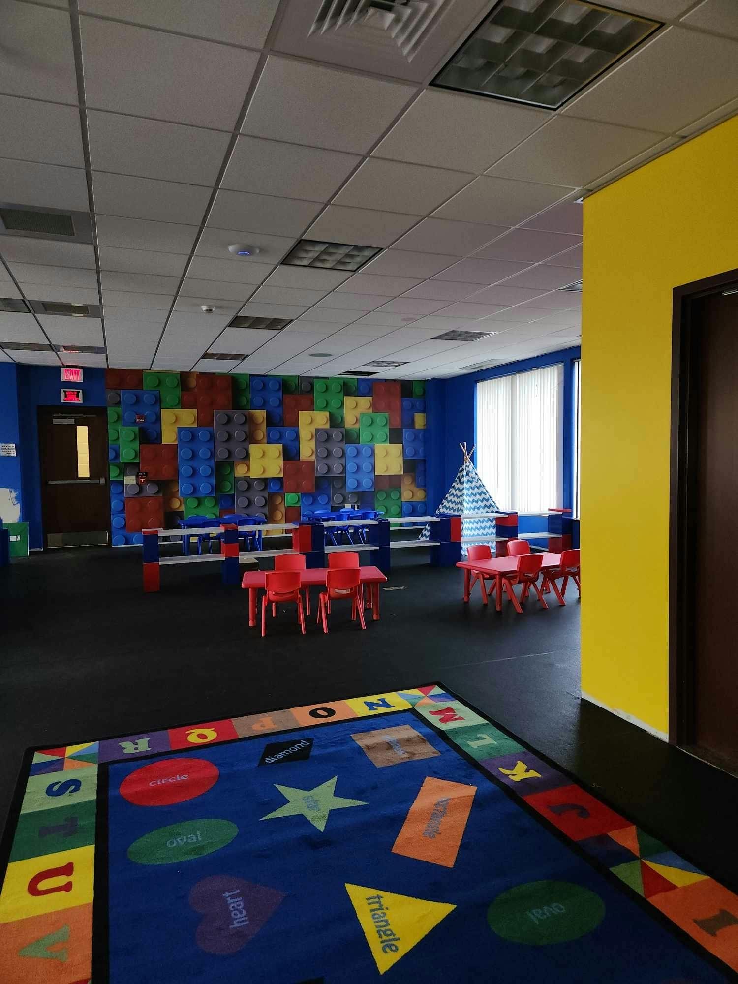 Playroom with colorful rug, small red tables and chairs, and a teepee