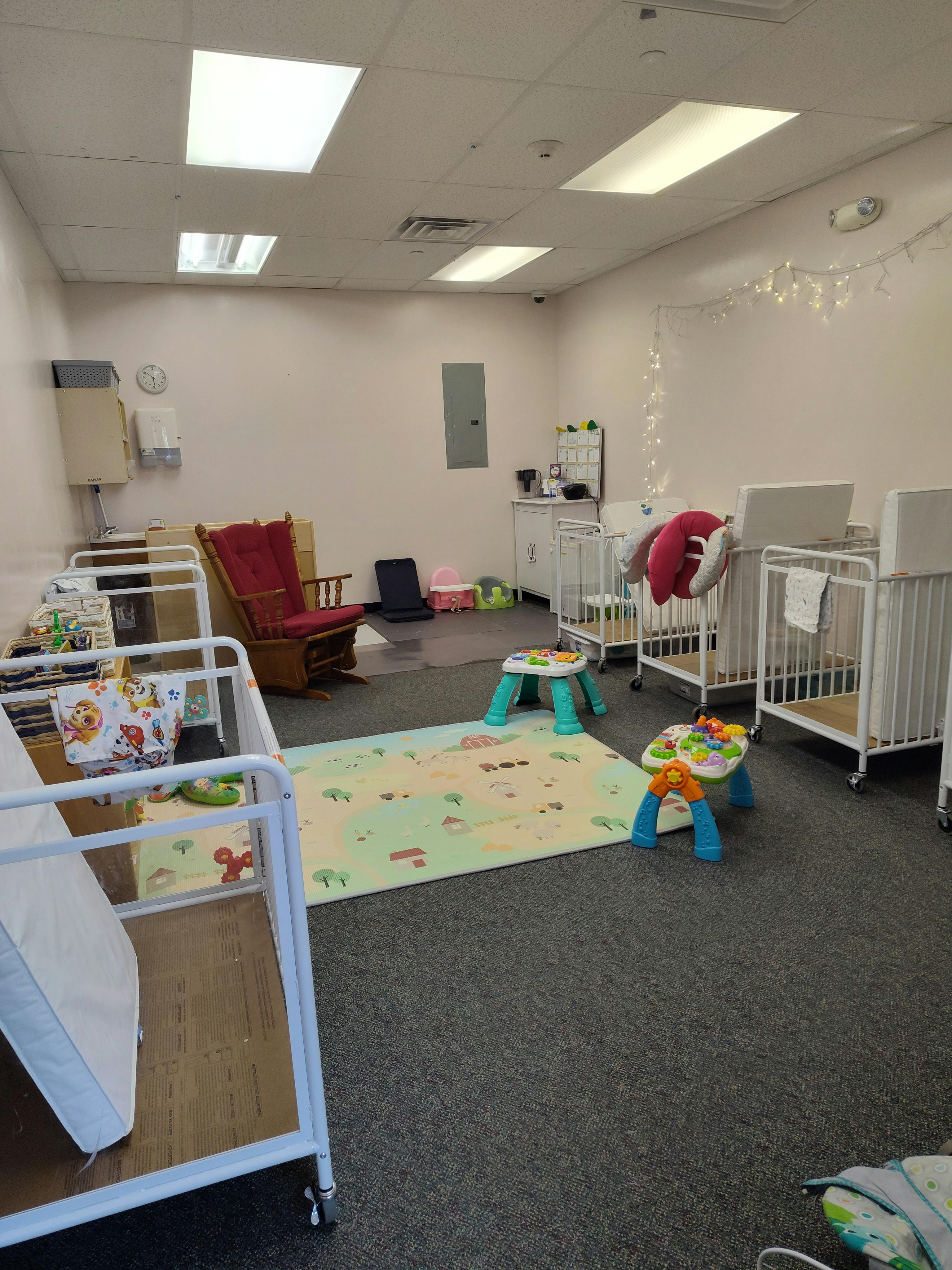 Nursery room with multiple cribs, a rocking chair, and play mats