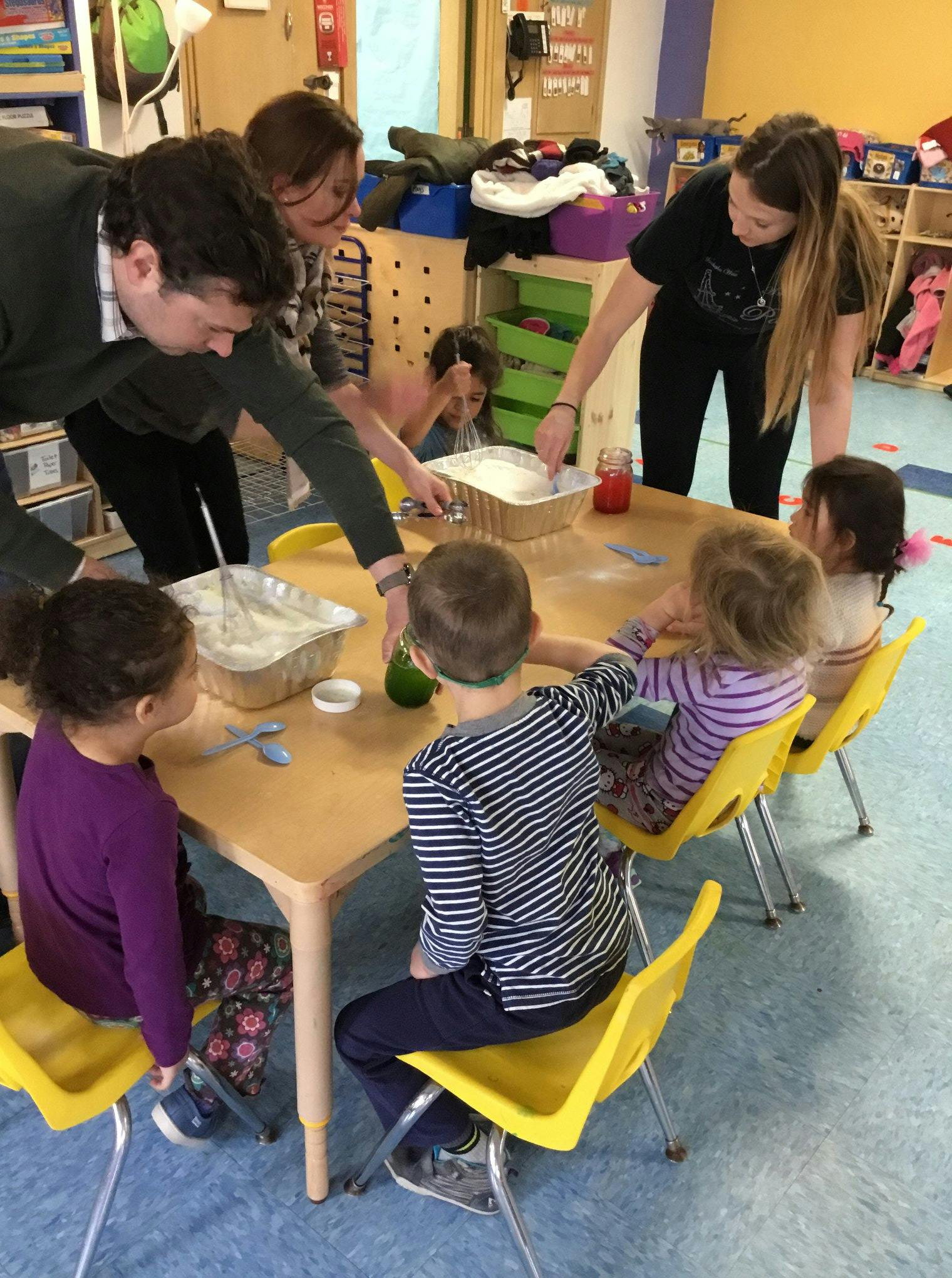 Adults and children gathered around a table with containers of bowls of ingredients