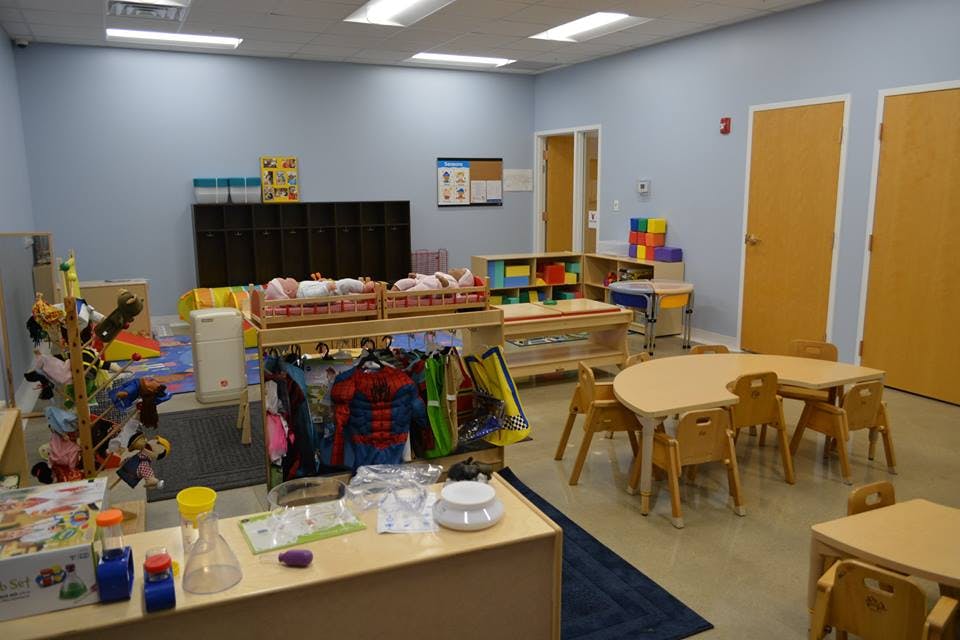 Classroom with small tables and chairs, shelves with toys, and clothes on a rack