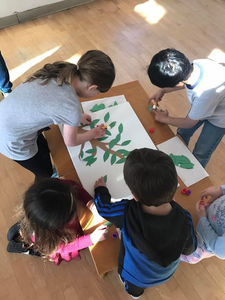 Children and an adult making a tree craft with paper leaves