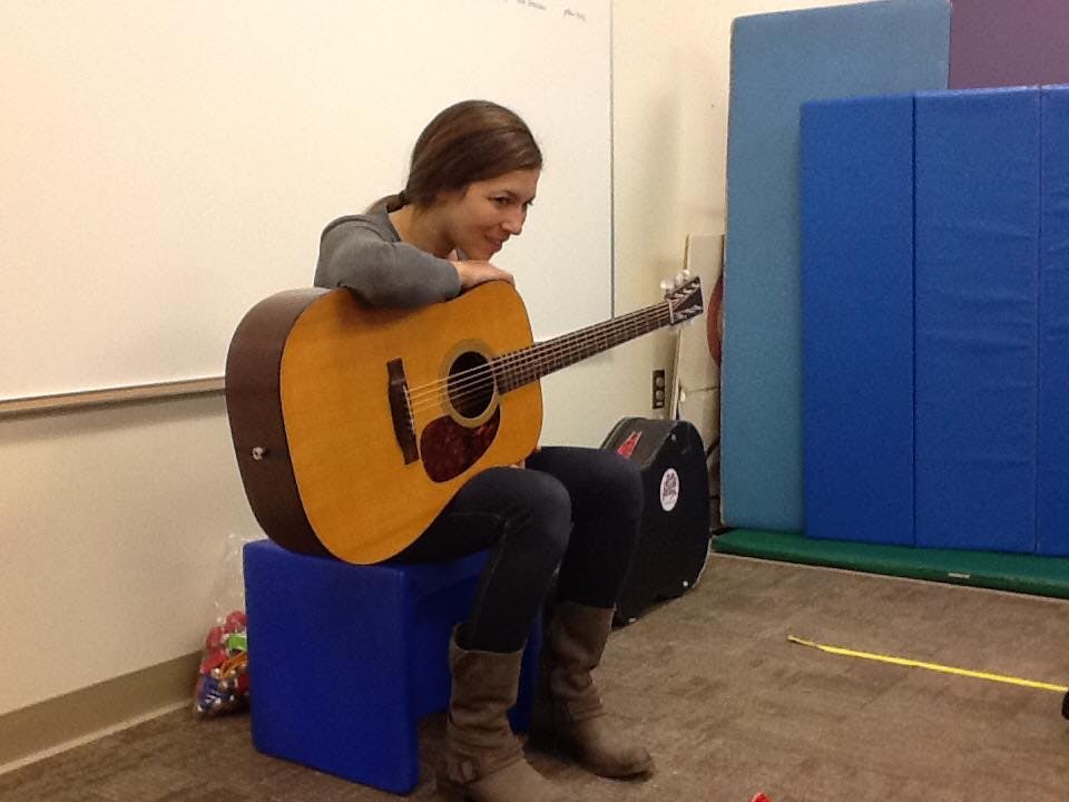 Person sitting on a blue block with a guitar