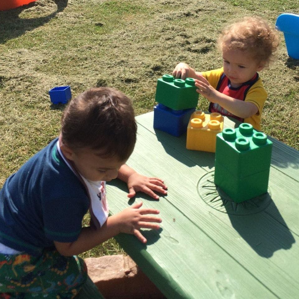 Two children playing with large building blocks on a table