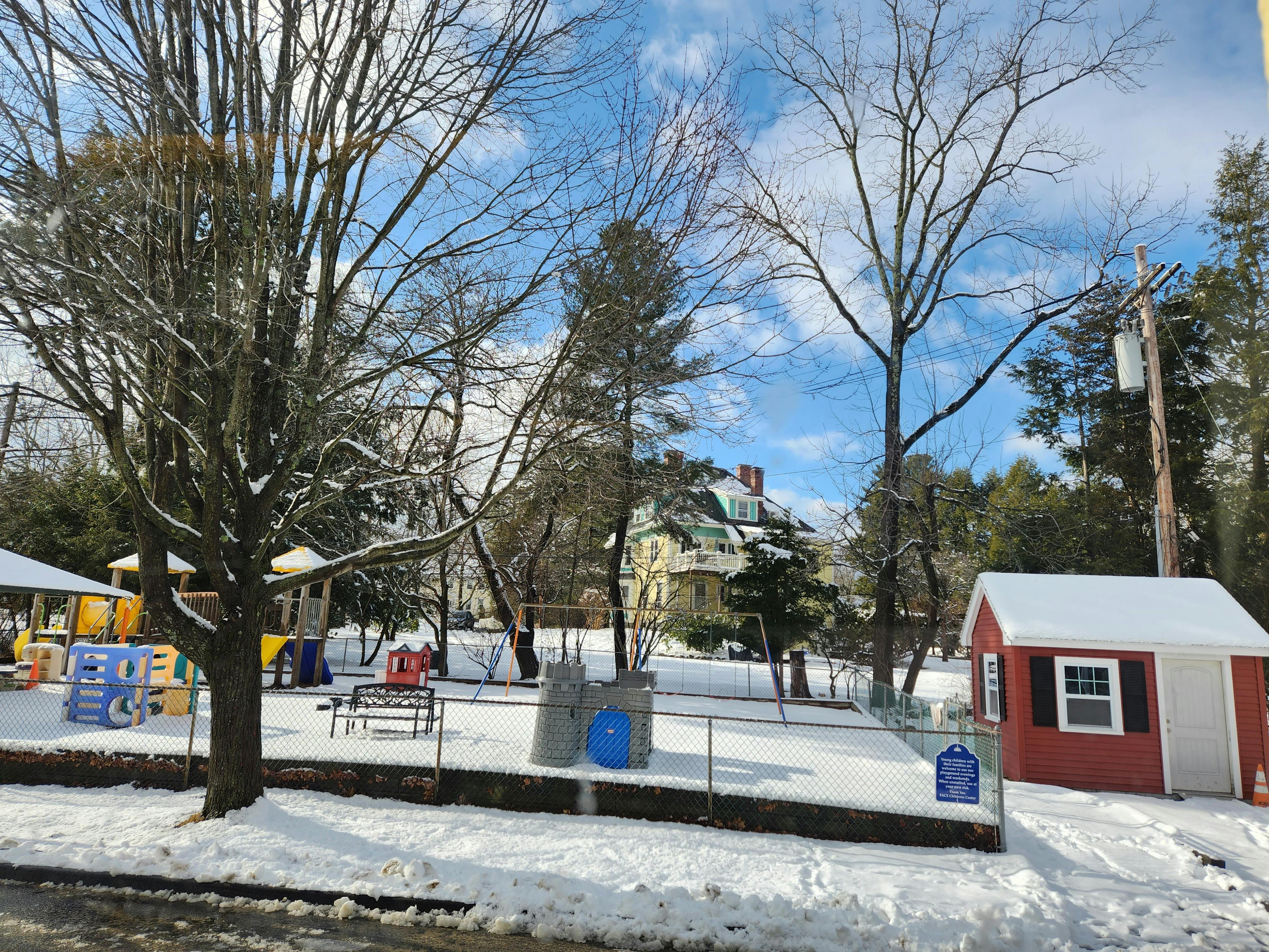 Snow-covered playground with bare trees and a small red shed