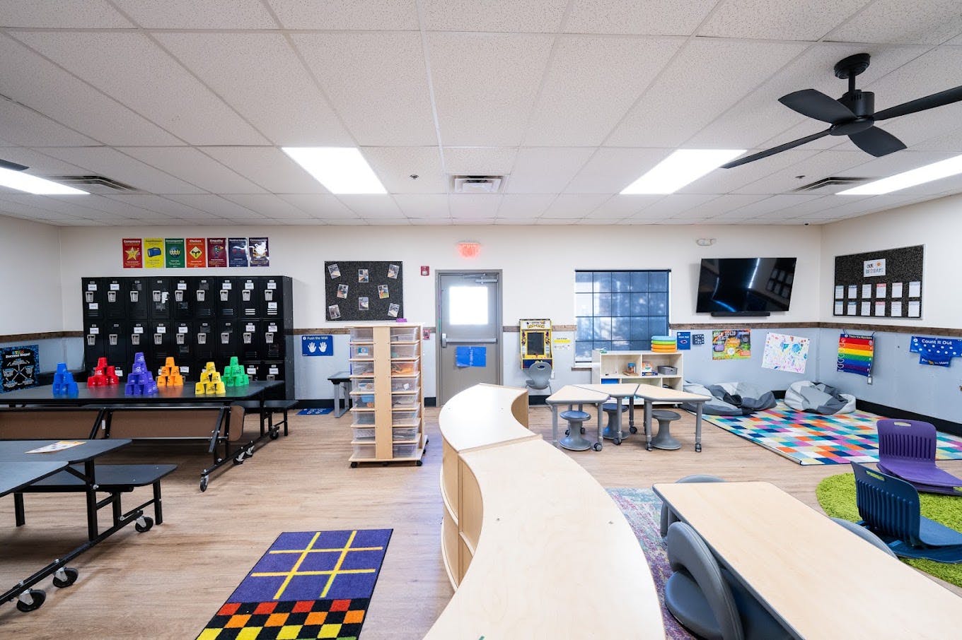 Classroom interior with tables, lockers, storage shelves, and colorful rugs