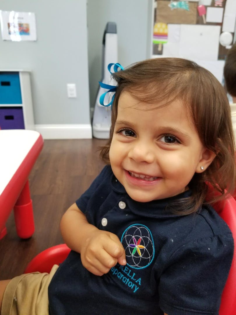 Child in a blue shirt with a logo, smiling at the camera