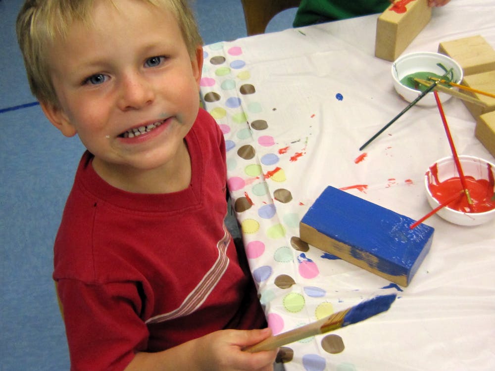 Child holding a paintbrush at a table with paint and blocks
