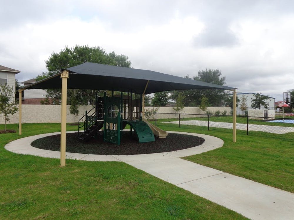 Playground with green slides and climbing structure under a shade canopy