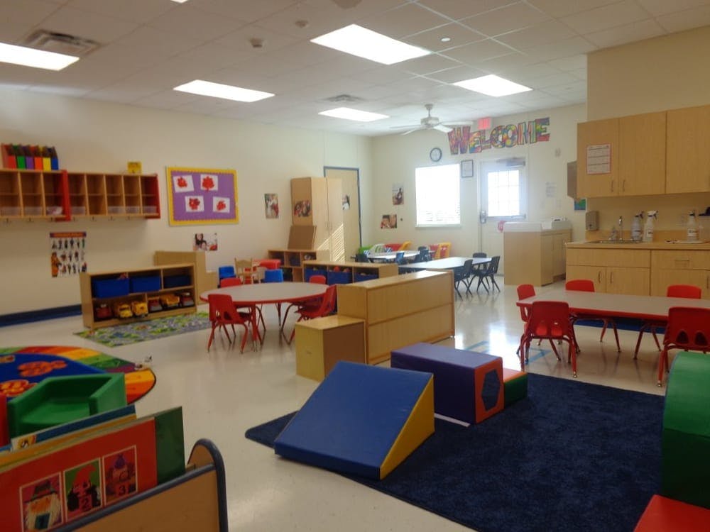 Empty classroom with small tables and chairs, storage units, and soft play equipment