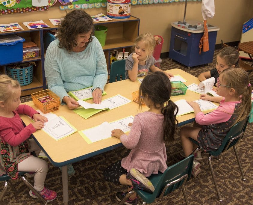Adult and multiple children sitting at a table with papers