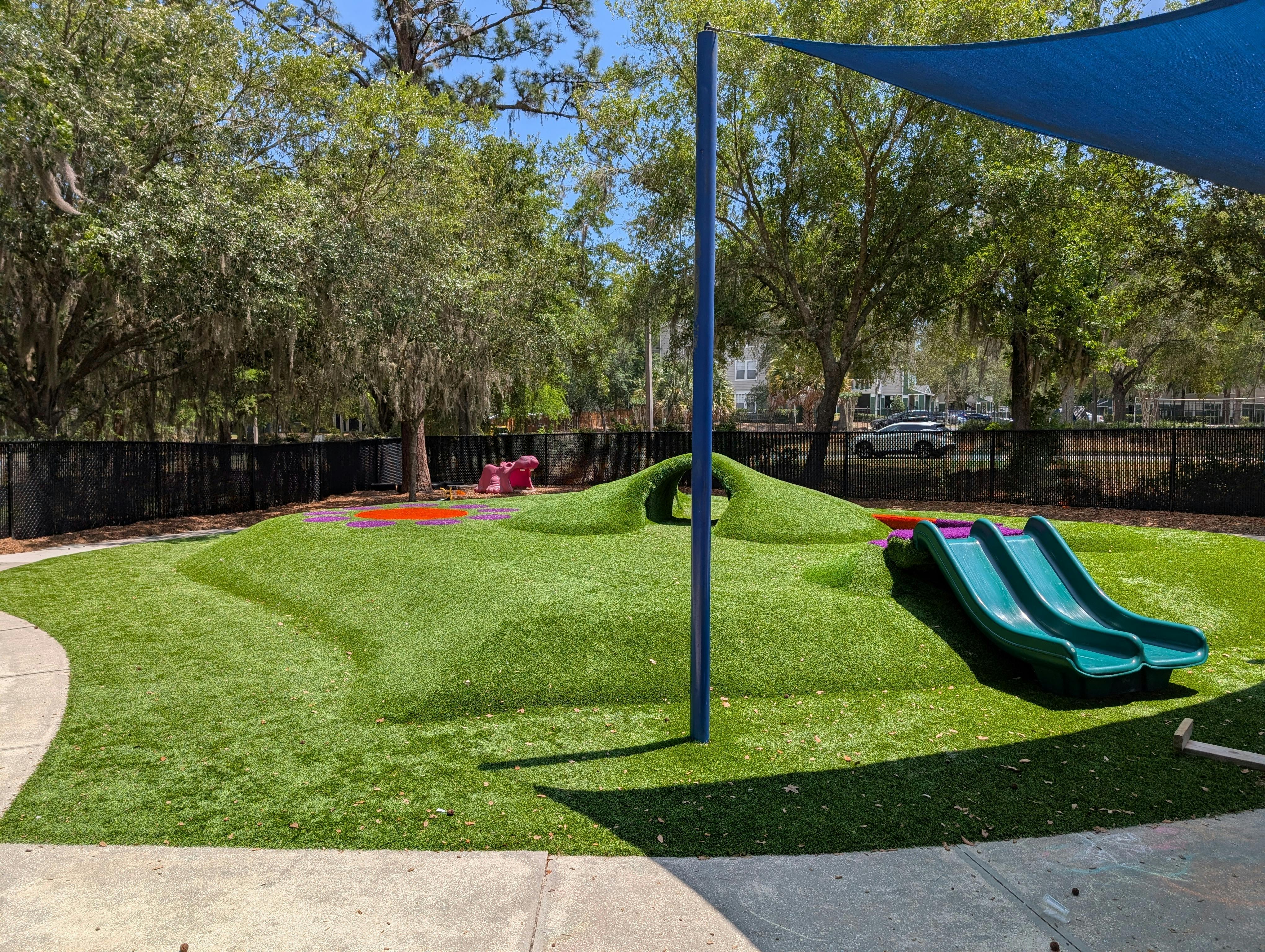 Playground with green turf, two slides, a play tunnel, and a pink hippopotamus