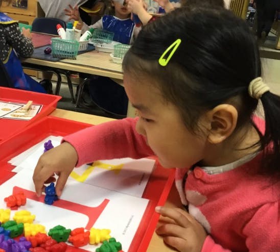 Child placing small colorful objects on a paper in a red tray