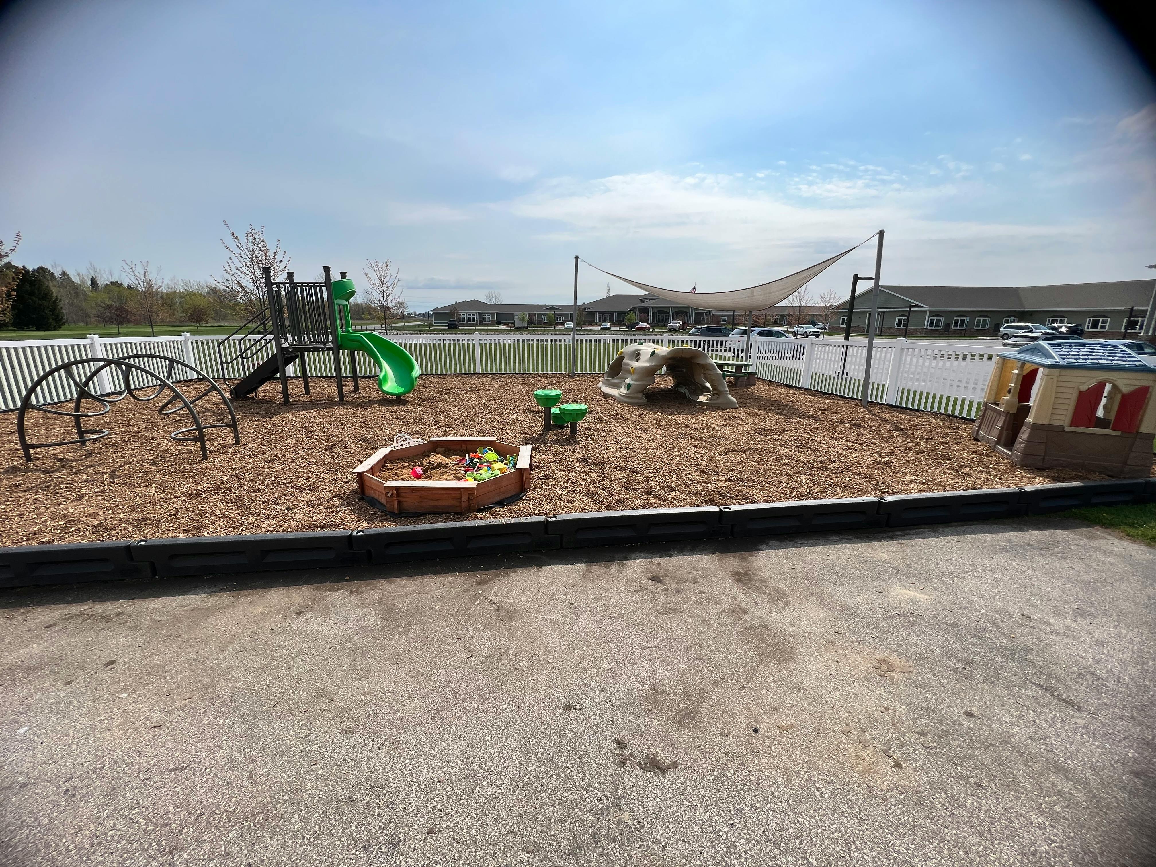Outdoor playground with slide, climbing dome, sandbox, and playhouse