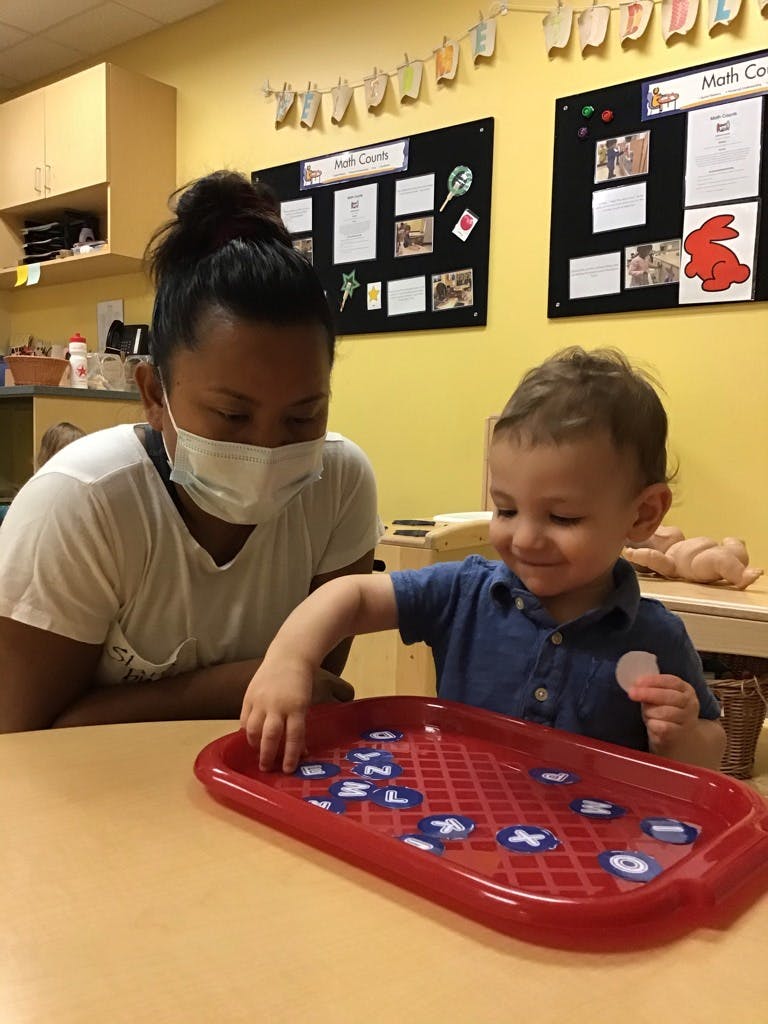Person in mask and child playing with letters on a red tray