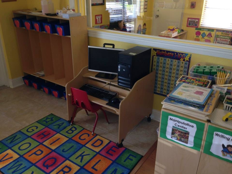 Computer desk with a red chair and an alphabet rug in a classroom