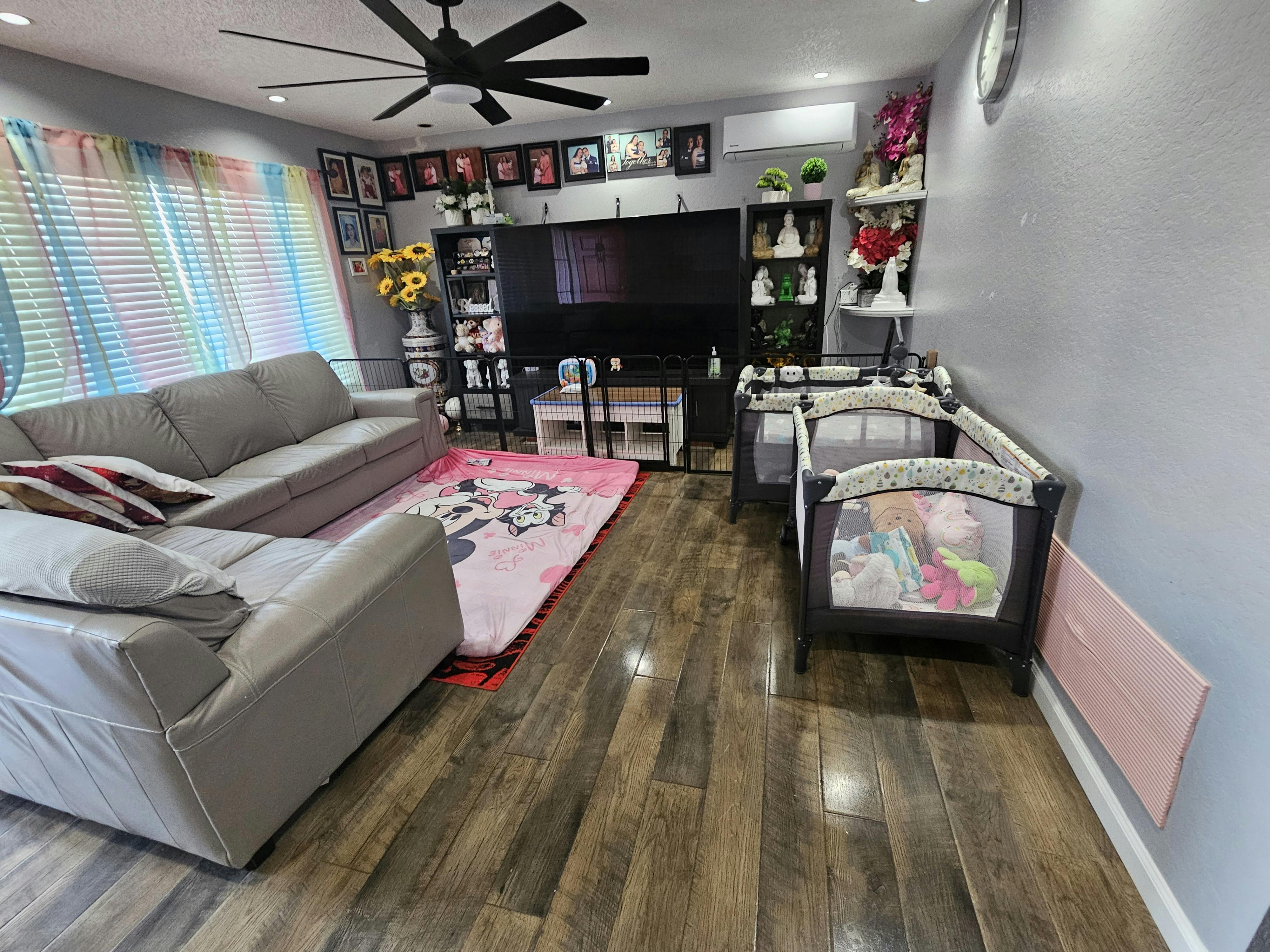 Living room with a gray sectional sofa, pink rug, and two playpens