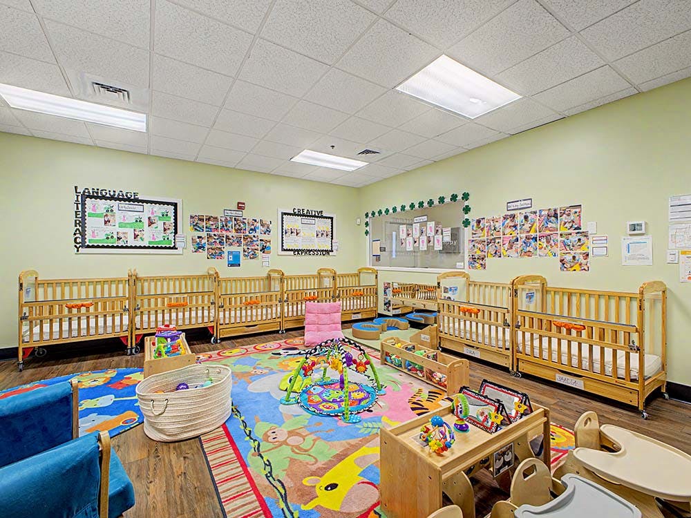 A colorful daycare classroom with multiple wooden cribs and play areas