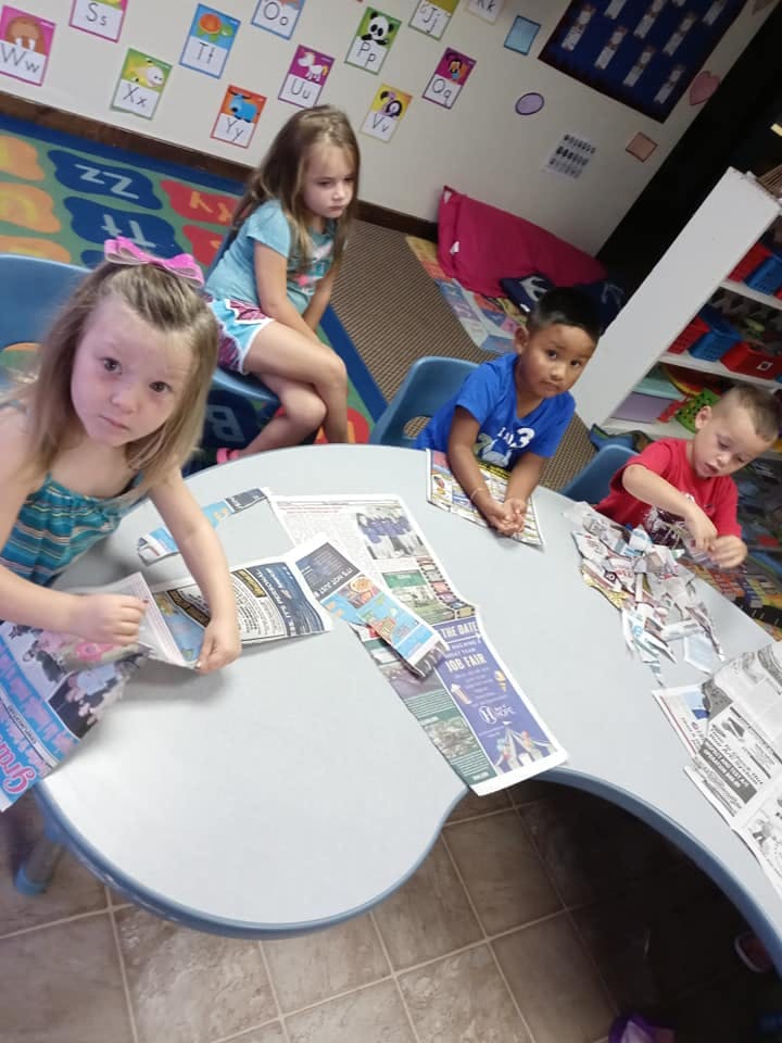 Four children sitting at a table with newspapers