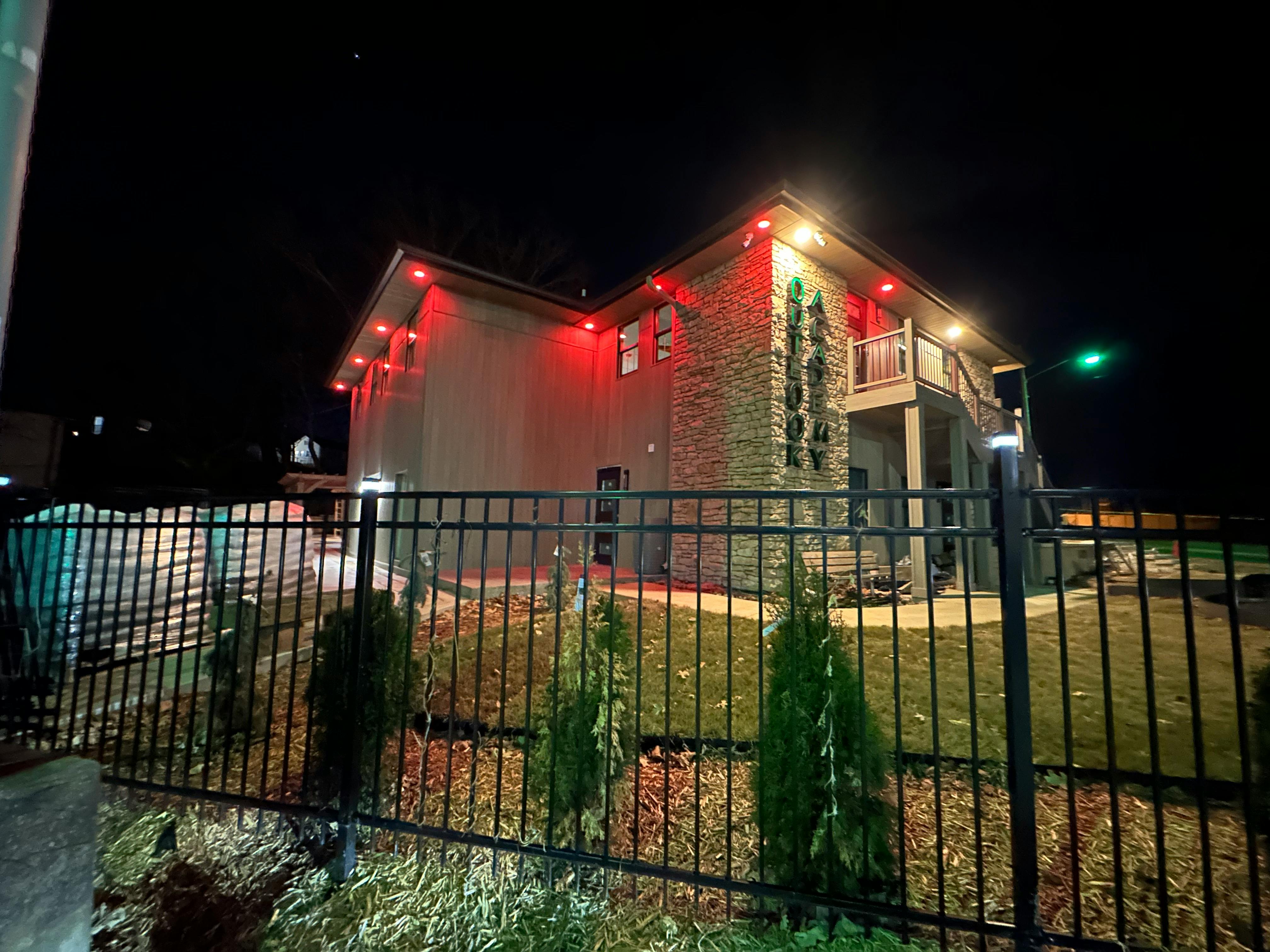 Building with red lights on the roofline at night behind a black fence