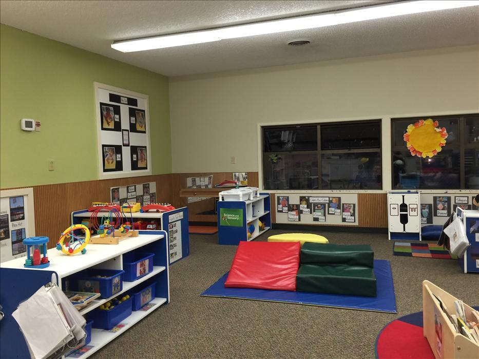 Classroom with shelves of toys, padded mats, and windows decorated with art