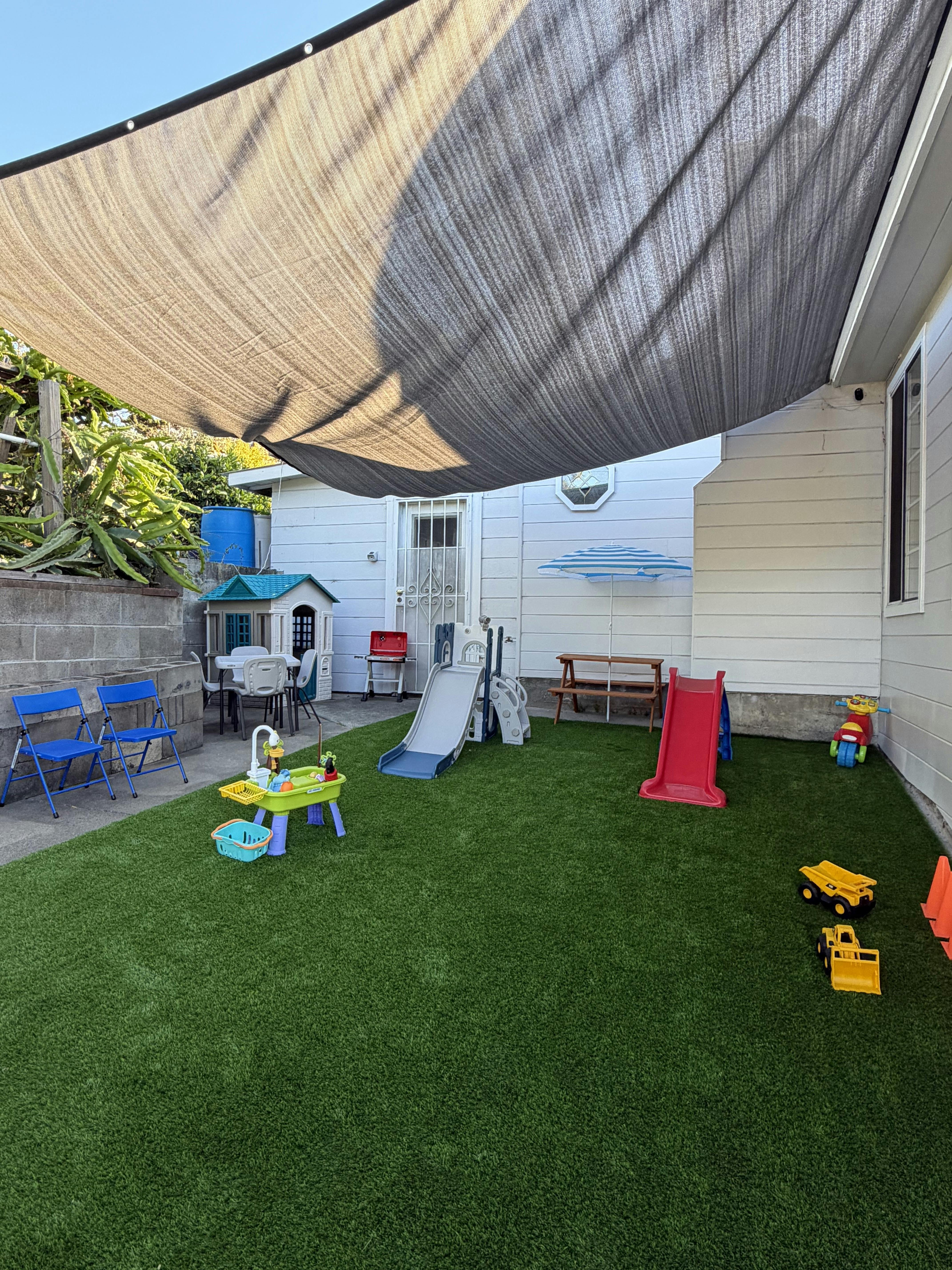Childrens play area with slides and toys on artificial grass under a shade sail