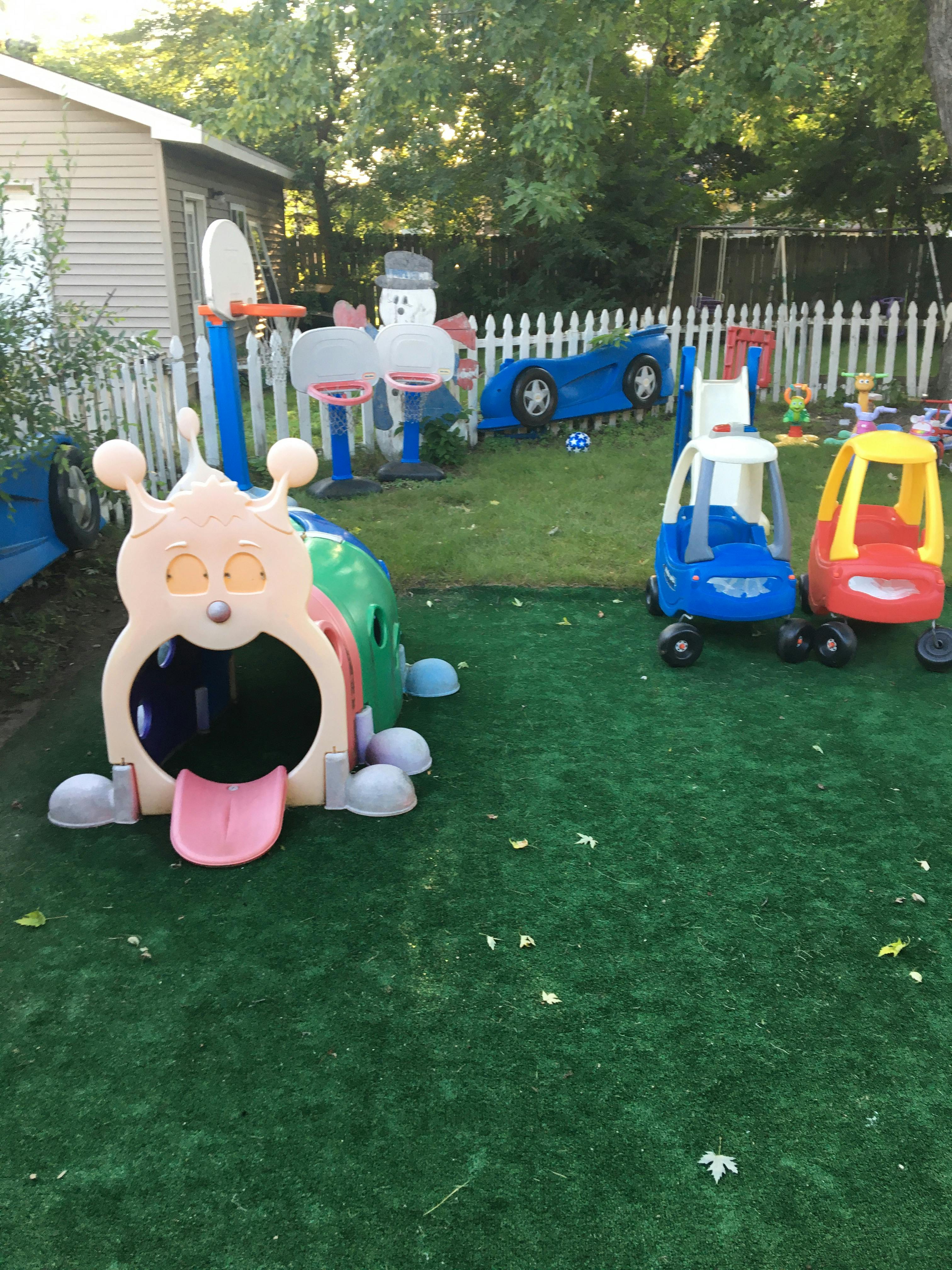 Outdoor play area with a caterpillar tunnel, toy cars, and a basketball hoop