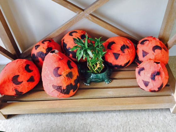 Orange paper mache pumpkins with black jack-o'-lantern faces and a plant