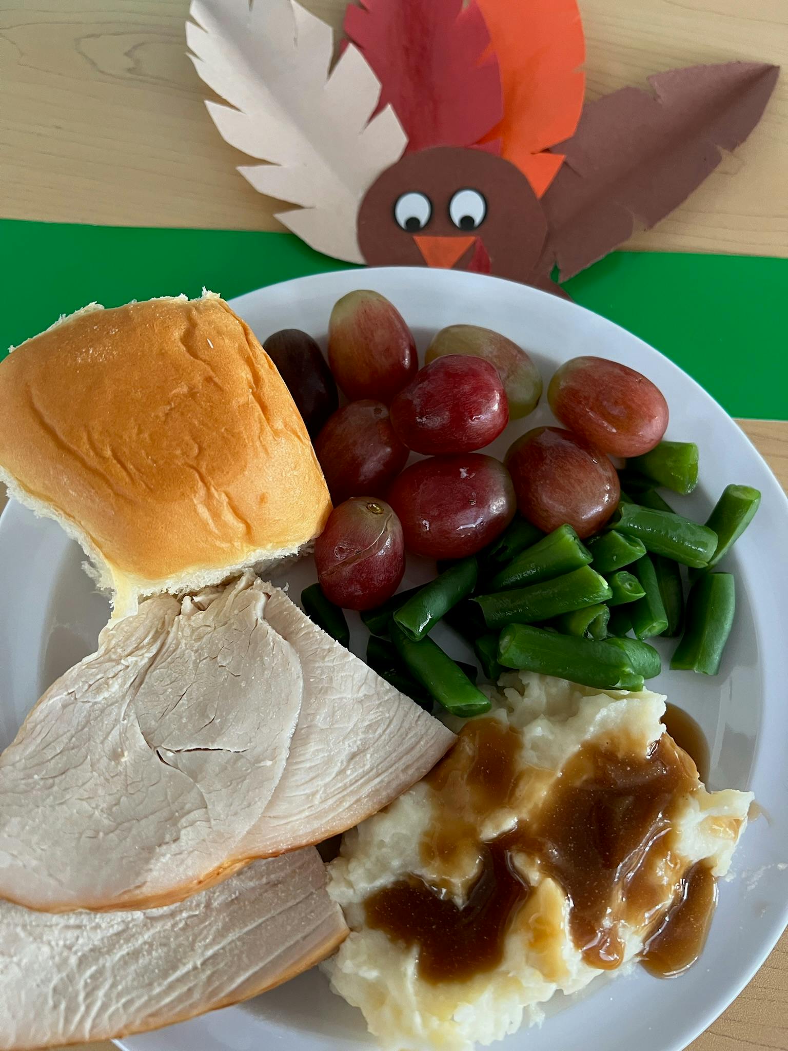 Plate of turkey, mashed potatoes, green beans, grapes, and a roll with a paper turkey