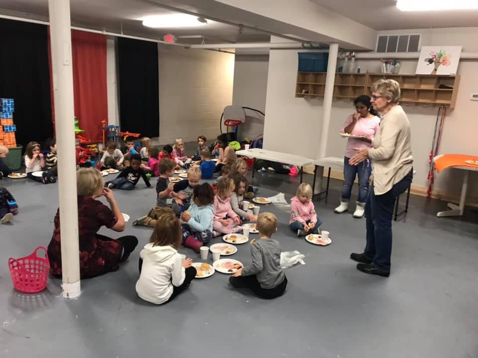 Adults and children sitting on the floor eating snacks