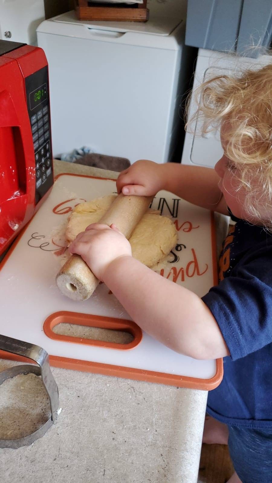 Child rolling dough on a cutting board in a kitchen
