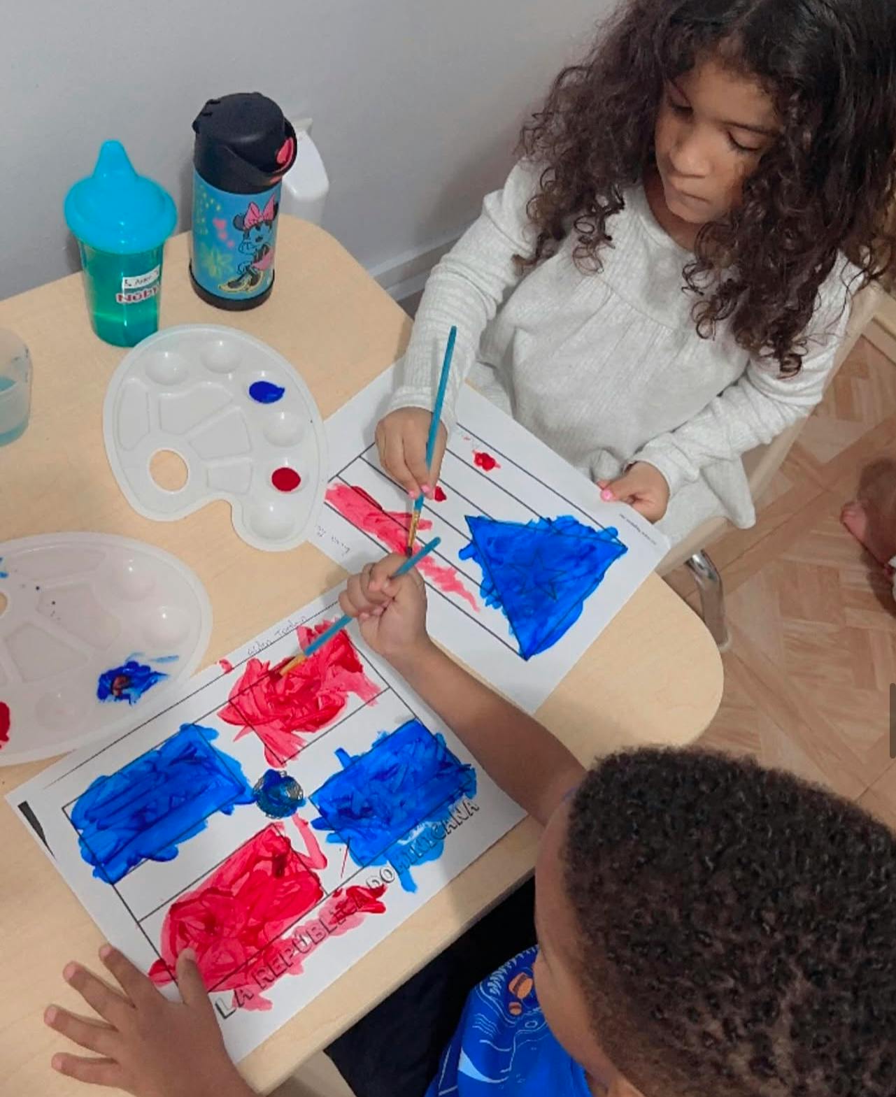 Two children painting with red and blue paint on paper