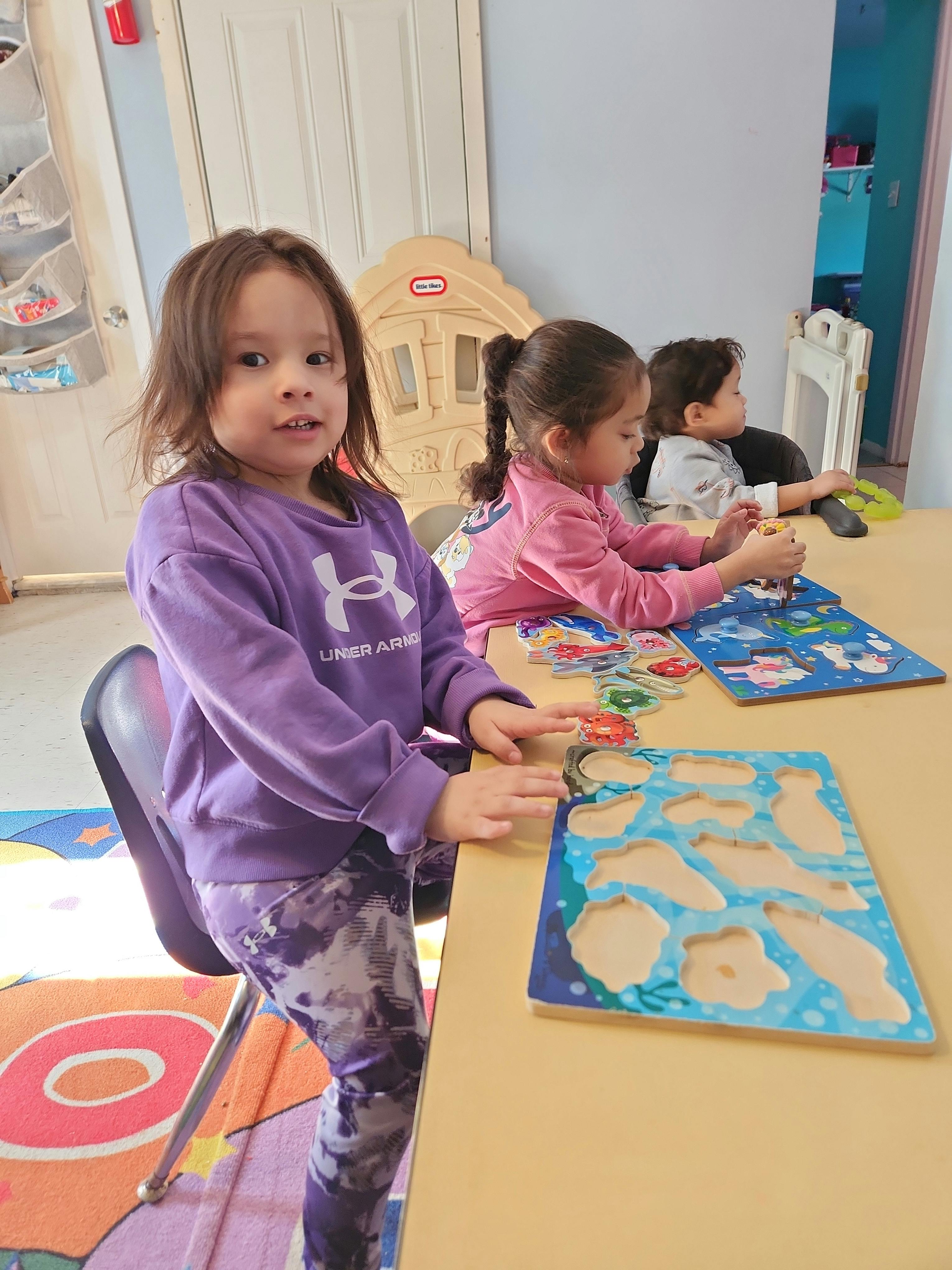 Child sitting at a table with a puzzle, looking forward