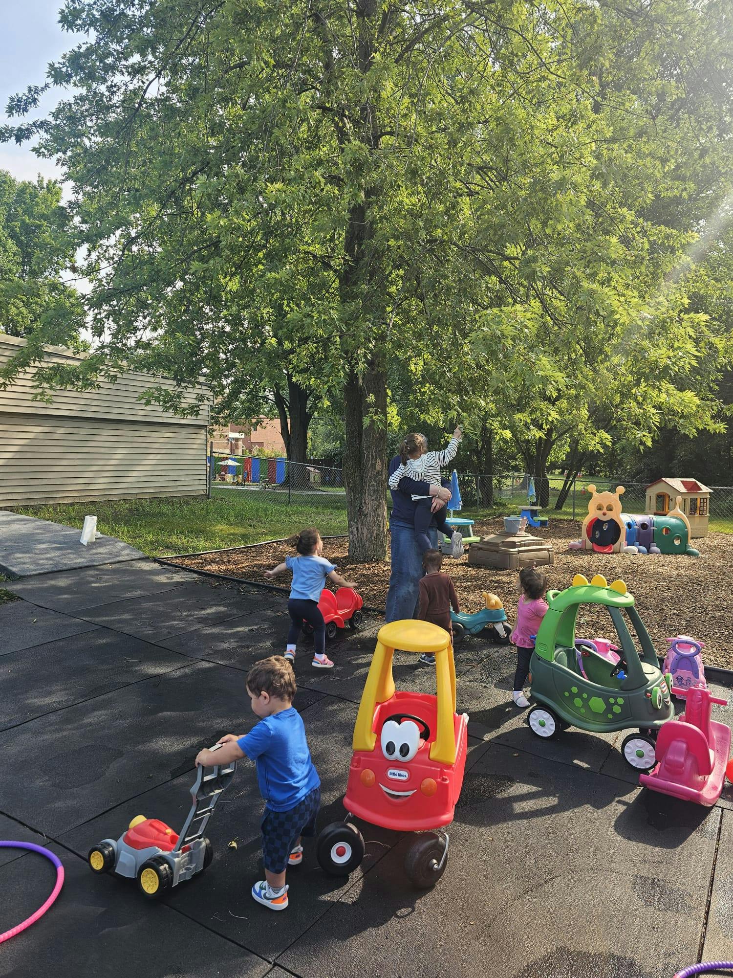 Children playing with toy cars and a toy lawnmower on a playground