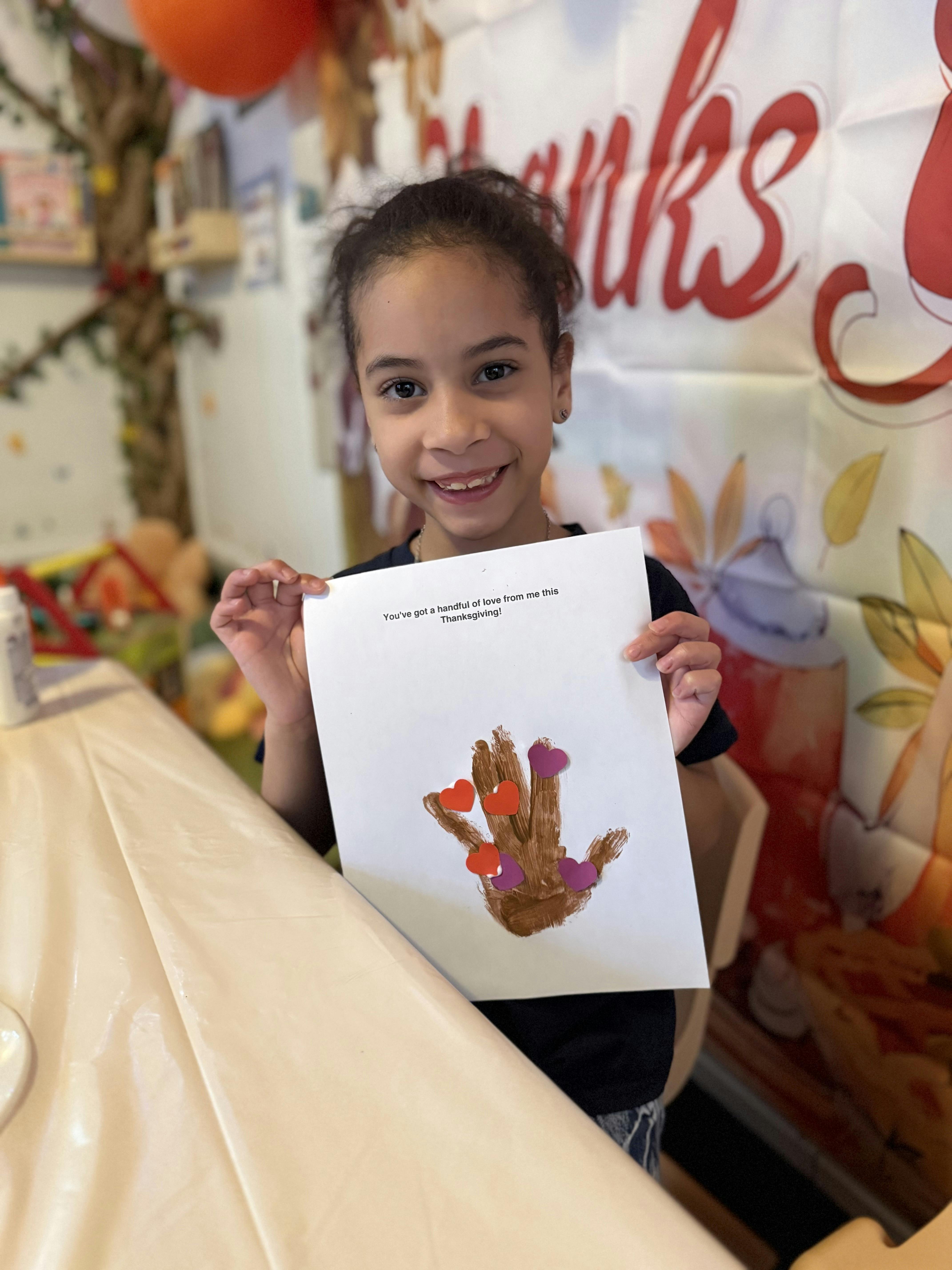 Child holding up a paper with a painted handprint and hearts