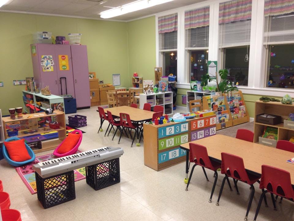 Classroom with small tables and chairs, shelves with toys, and a keyboard