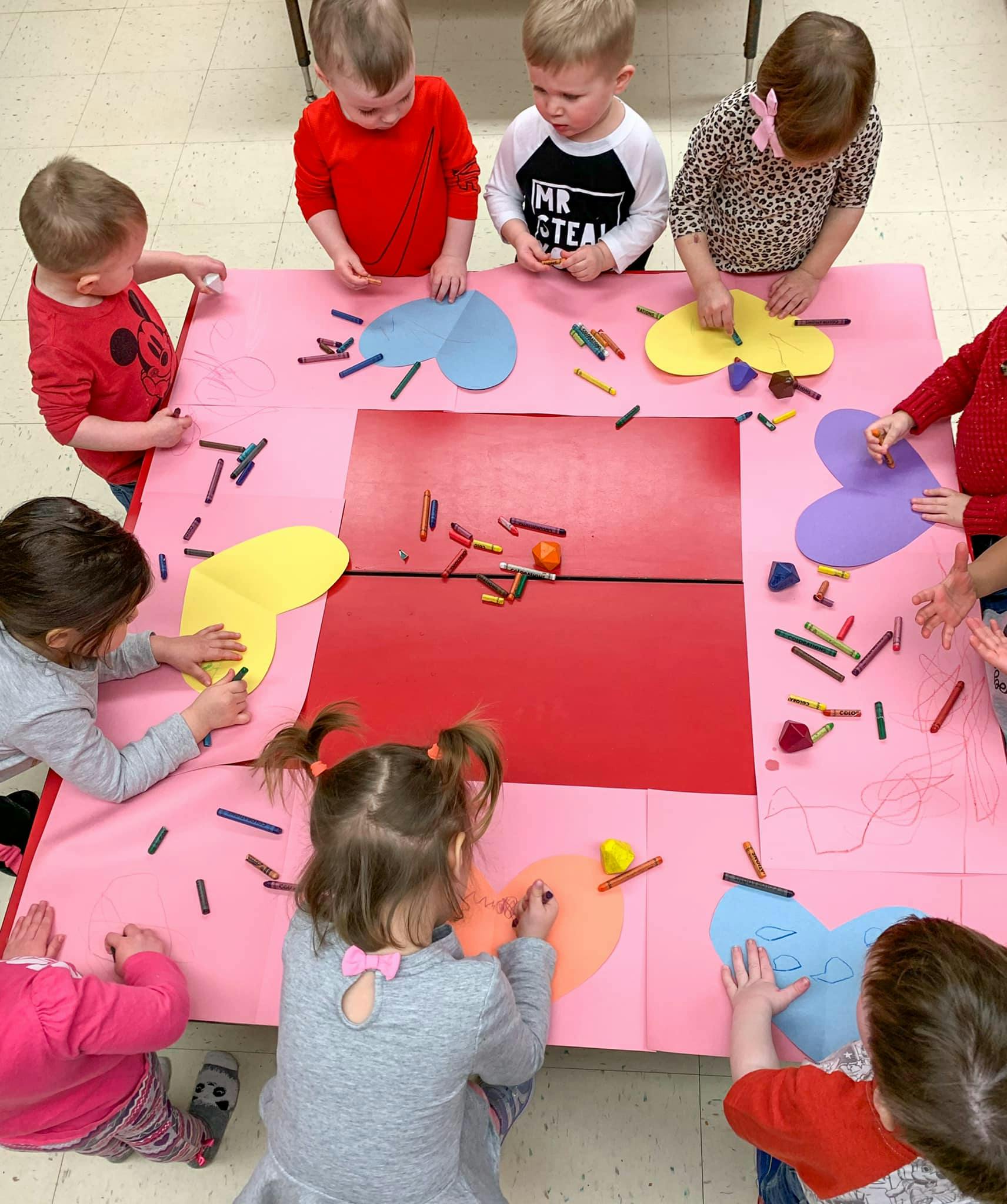 Children coloring heart shapes on a large pink paper