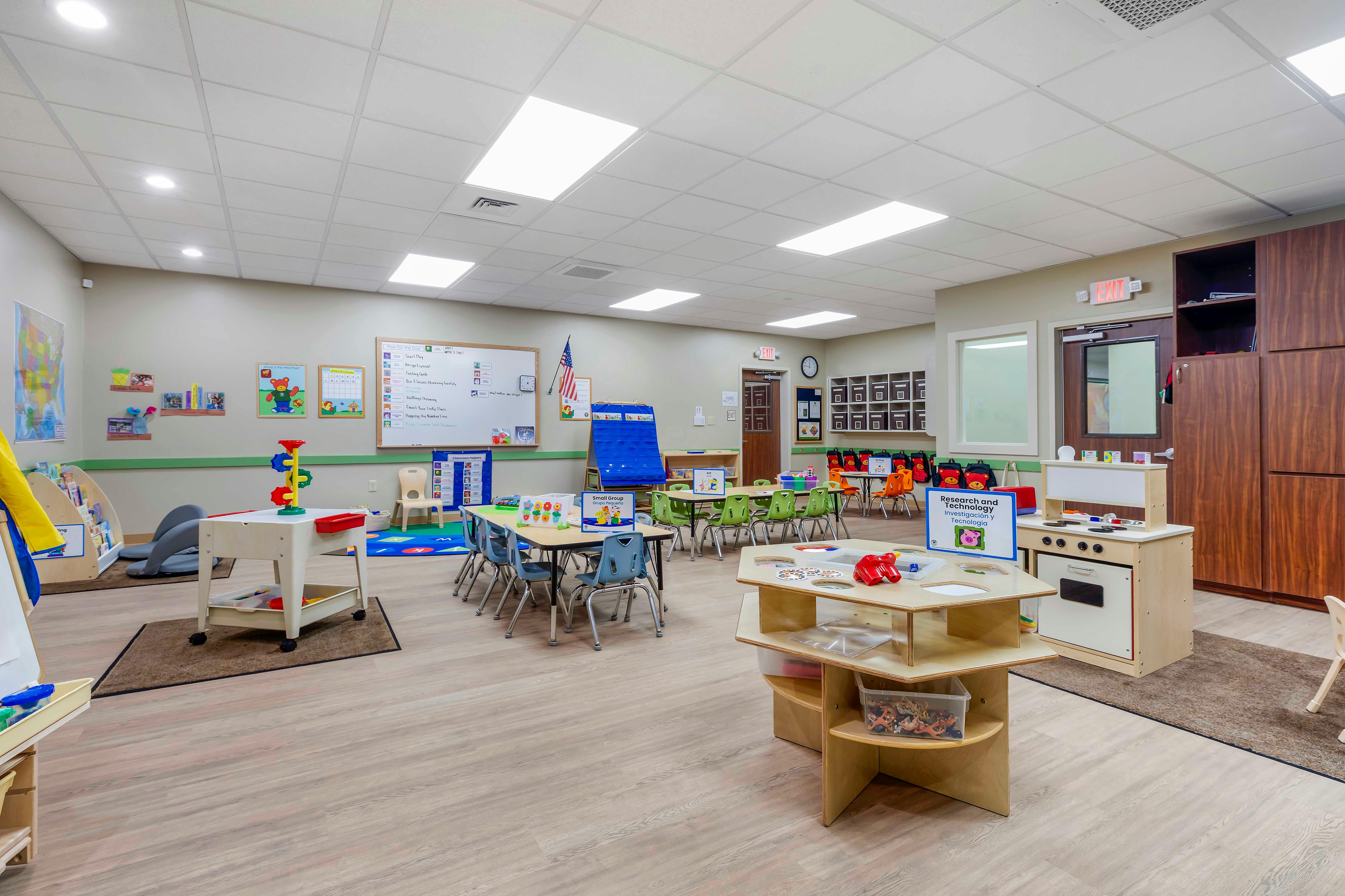 An empty preschool classroom with small tables and chairs, toys, and educational posters