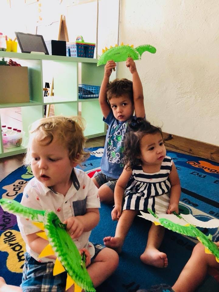 Three children sitting on a rug, two holding green paper crafts