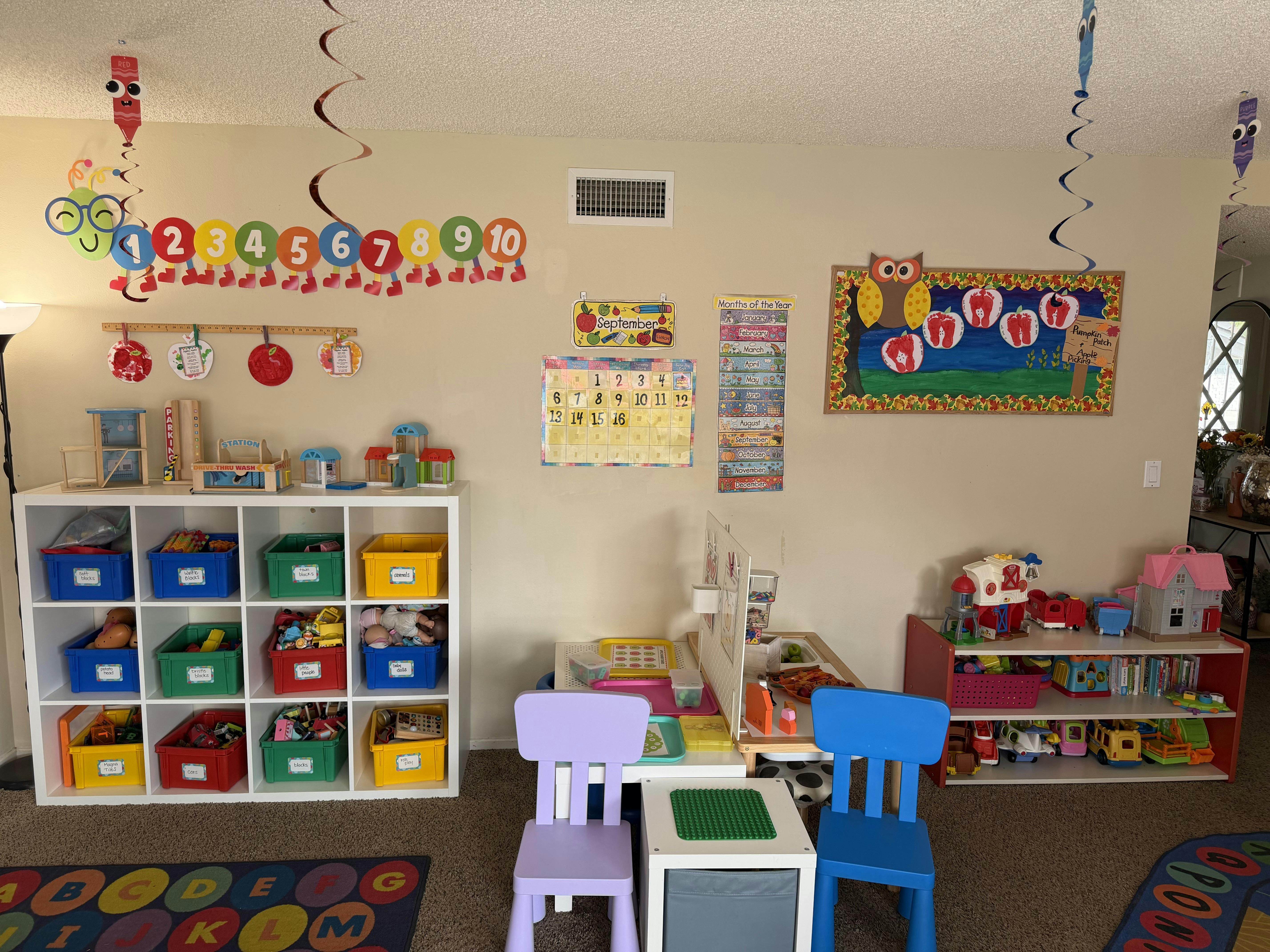Classroom interior with toy storage shelves, activity tables, and wall charts