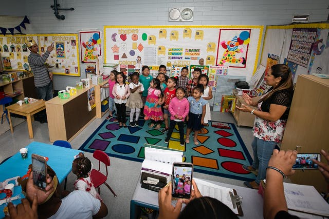 Adults filming a group of children standing on a rug in a classroom