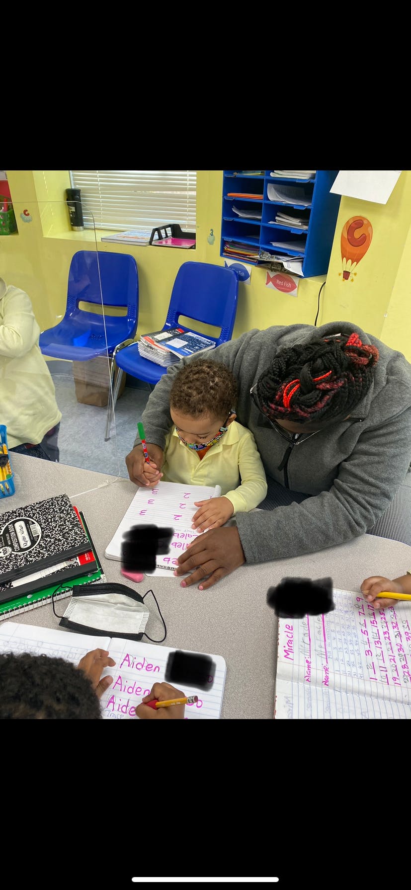 Person and child writing at a table in a classroom