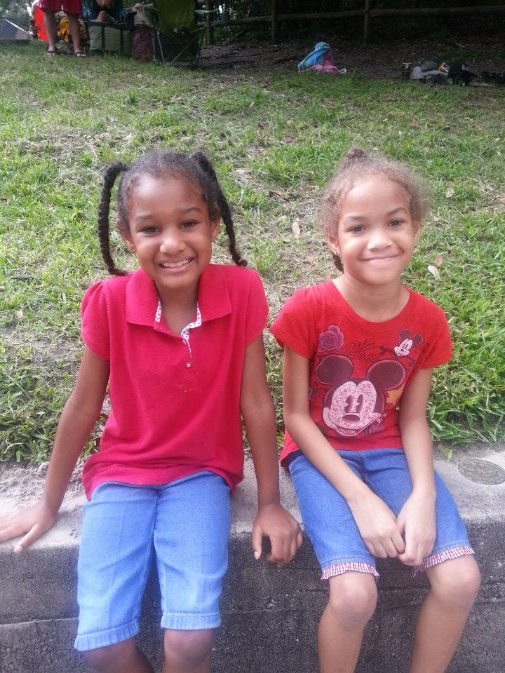Two children in red shirts and blue shorts sitting side by side