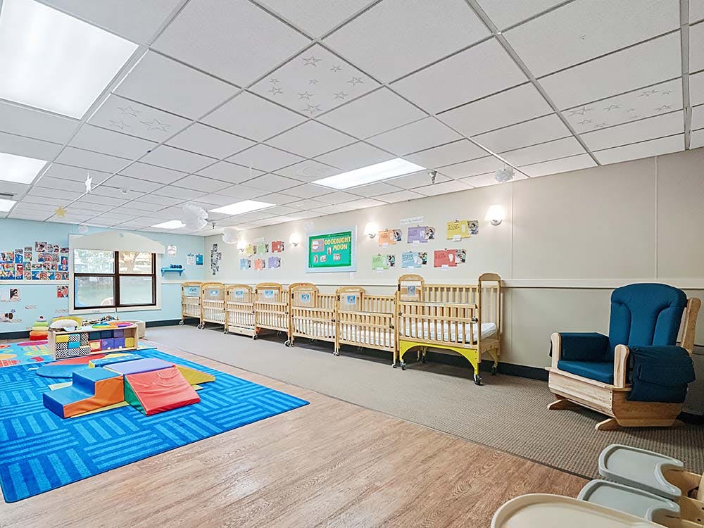 cribs in a daycare room with a play area and rocking chair